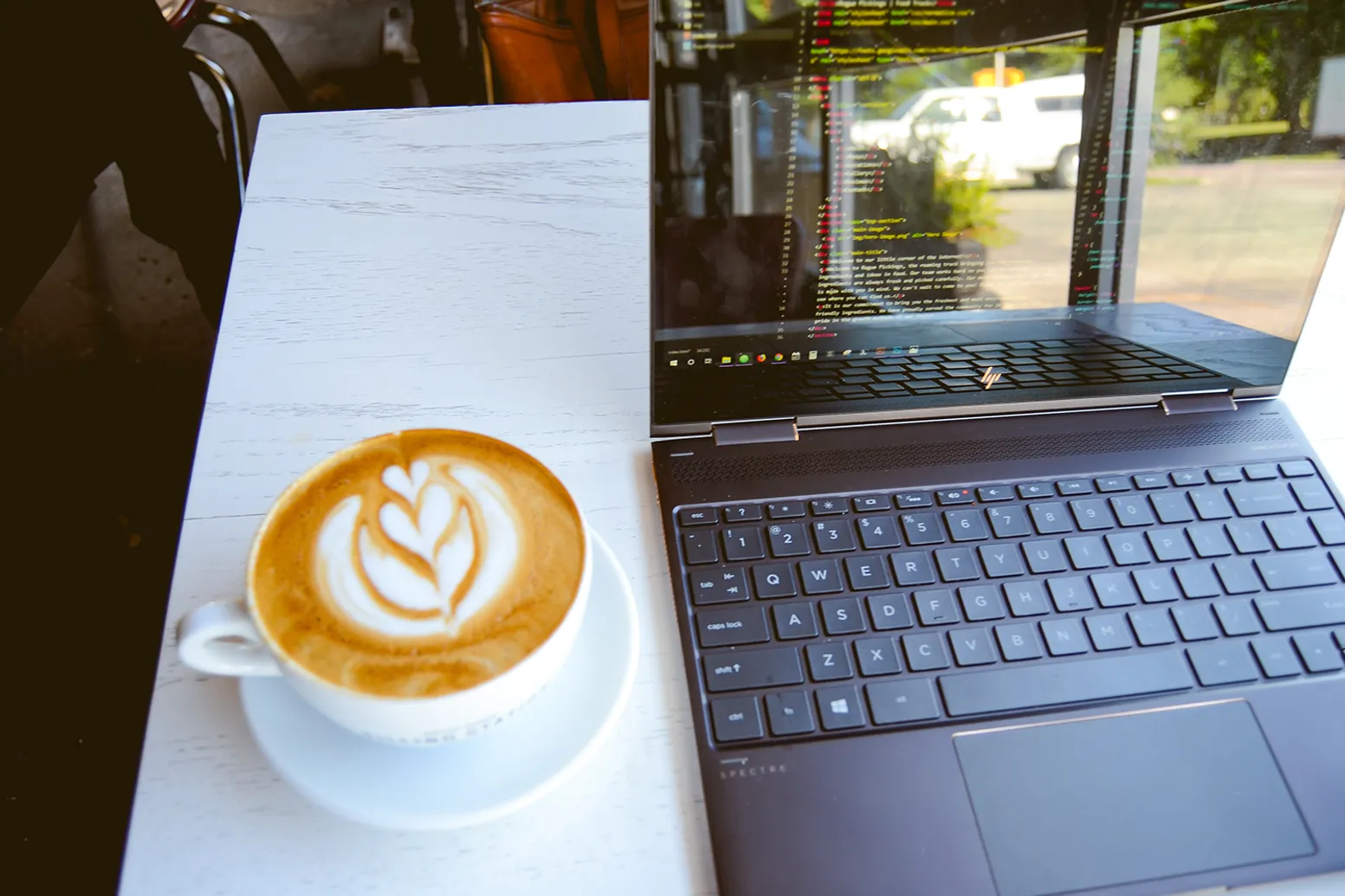 Picture of an open laptop and a capuccino on top of a white table